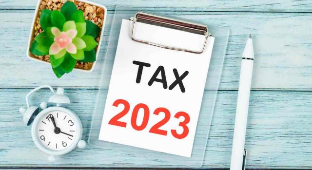 Modelo 390. Un portafolios con el texto Tax 2023, al lado un despertador, un bolígrafo y una planta