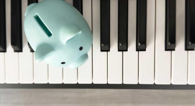 La Comunidad Valenciana aprueba una nueva deducción aplicable a IRPF para sufragar los gastos efectuados en actividades vinculadas a la formación y práctica musicales. Imagen del teclado de un piano en el que encima tiene un cerdito de ahorro en azul clarito