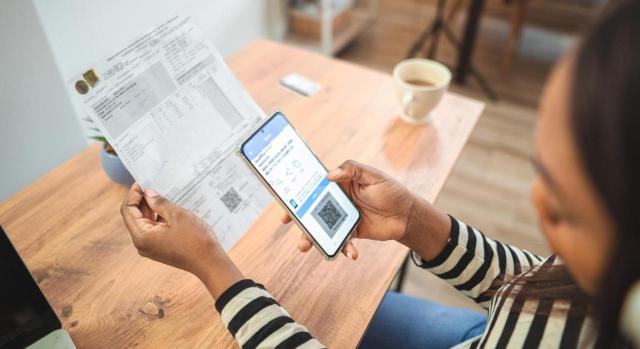 Diferencias entre Veri*factu y el SII y ventajas y desventajas de cada sistema Diferencias entre Veri*factu y el SII y ventajas y desventajas de cada sistema. Mujer escaneando código qr en factura de papel con teléfono inteligente