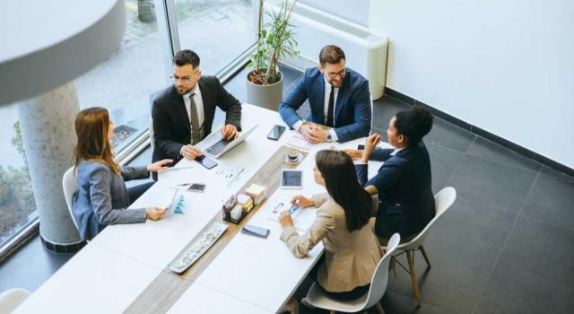 Régimen especial de grupo de entidades IVA: cesión o arrendamiento de inmuebles Efectos de la aplicación del régimen especial del grupo de entidades del IVA en su nivel avanzado, en relación con la cesión o el arrendamiento de un inmueble. Imagen de una vista aérea de una reunión de trabjao de cinco personas